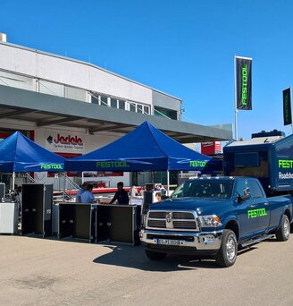 Gazebo per eventi 3x3m blu personalizzati con logo verde Festool abbinati a furgoncino e caravan aziendali davanti negozio di fai da te Jedele