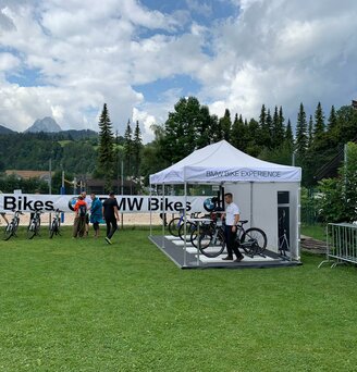 Weißer 6x3 Faltpavillon mit BMW Bike experience Schriftzug und Seitenwand auf einer Wiese mit Baum- und Bergkulisse 
