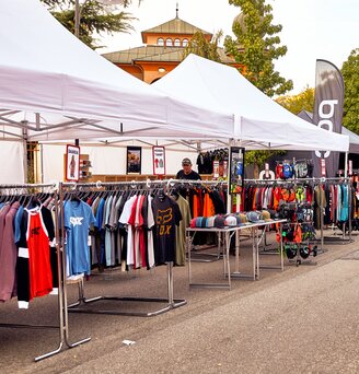 Die weißen Promotionzelte dienen als Verkaufszelt auf einem Event. Unter dem Faltpavillon hängen verschiedene T-shirts.