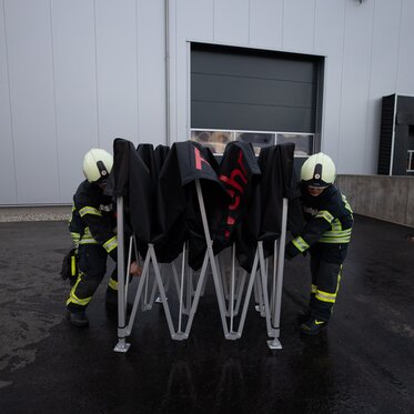 Vigili del fuoco di Ulm in Germania aprono un gazebo pieghevole 3x3m nero Ecotent personalizzato con scritta rossa durante un'emergenza