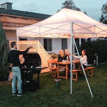 Gli amici festeggiano un barbecue e una festa in giardino sotto il gazebo da giardino. Il gazebo è decorato a festa con luci fiabesche.