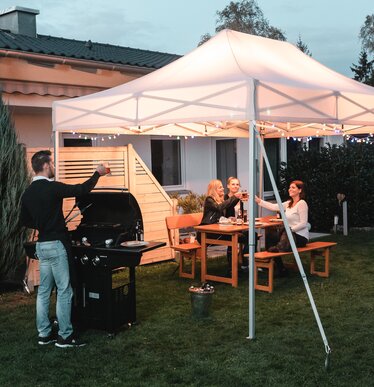 Gli amici festeggiano un barbecue e una festa in giardino sotto il gazebo da giardino. Il gazebo è decorato a festa con luci fiabesche.