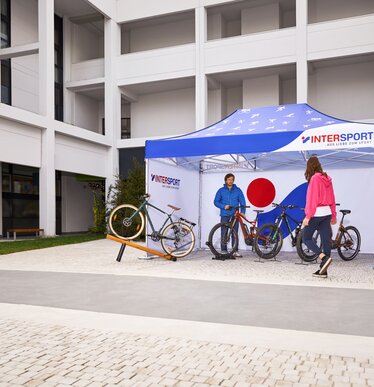 Das bedruckte Promotionzelt von "Intersport" steht auf dem Außengeländ der Messe. Unter dem 4,5x3 m großen Faltpavillon steht der Verkäufer und seine Fahrräder.