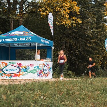 Il gazebo blu e bianca serve come stazione di rifornimento per la maratona. 2 atleti passano davanti al gazebo dell'evento.