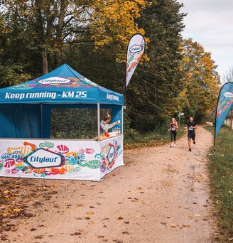 Il gazebo blu e bianca serve come stazione di rifornimento per la maratona. 2 atleti passano davanti al gazebo dell'evento.