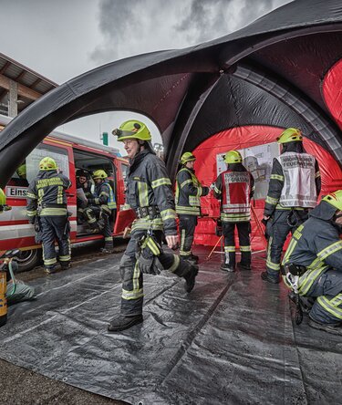 Squadra di vigili del fuoco al lavoro all’interno e davanti a un gazebo gonfiabile di emergenza rosso e nero accanto a un veicolo di soccorso.