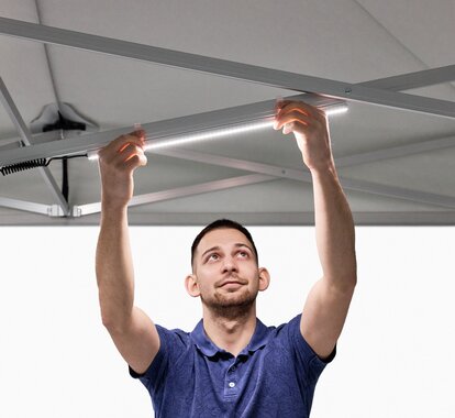 Der Mann bringt die LED-Leisten am Faltpavillon an.