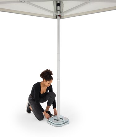 Die Frau hat zwei Bodenplatten am Faltpavillon angebracht. Eine mit 20 Kg und eine mit 10 Kg.