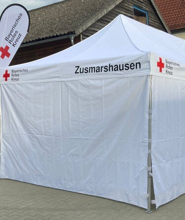 Weißes Faltzelt 6x4 m Ecotent® mit Aufdruck Bayerisches Rotes Kreuz, aufgestellt vom BRK Zusmarshausen als Sanitätszelt.