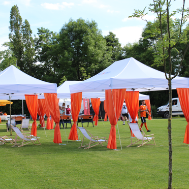 White Ecotent® 6x4 m pop-up gazebo with orange decorative curtains at an outdoor event with deck chairs.