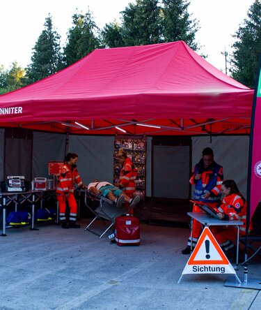 Gazebo per le emergenze 6x4 rosso con pareti laterali Rescue grige e due bandiere a goccia personalizzate con logo utilizzato per una simulazione di emergenzain fiera.