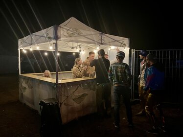 Ecotent® printed pop-up gazebo with leaf design, used as an outdoor bar at night with lights and people enjoying drinks.