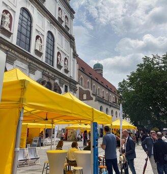 In einer Einkaufsstraße in München stehen mehrere gelbe Faltpavillons von Ecotent der Serie E1/E2 in der Größe 3x3 mit Seitenwänden.