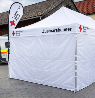 Faltpavillon 8x4 m weiß mit geschlossenen Seitenwänden und Seitenwänden mit Fenster, personalisiert mit dem Logo vom Bayersischen Roten Kreuz.
